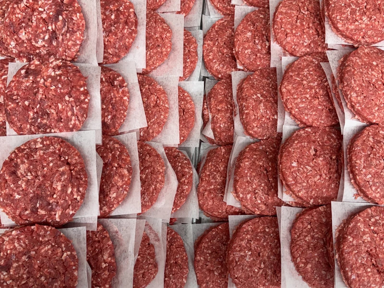 Hundreds of ground beef patties pressed and stacked between paper sheets