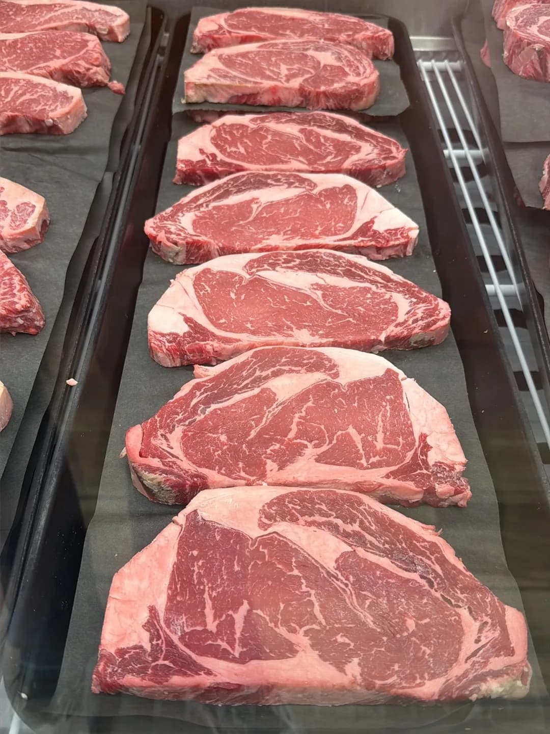 Fresh-cut ribeye and strip steaks laid out on trays in the cutting room