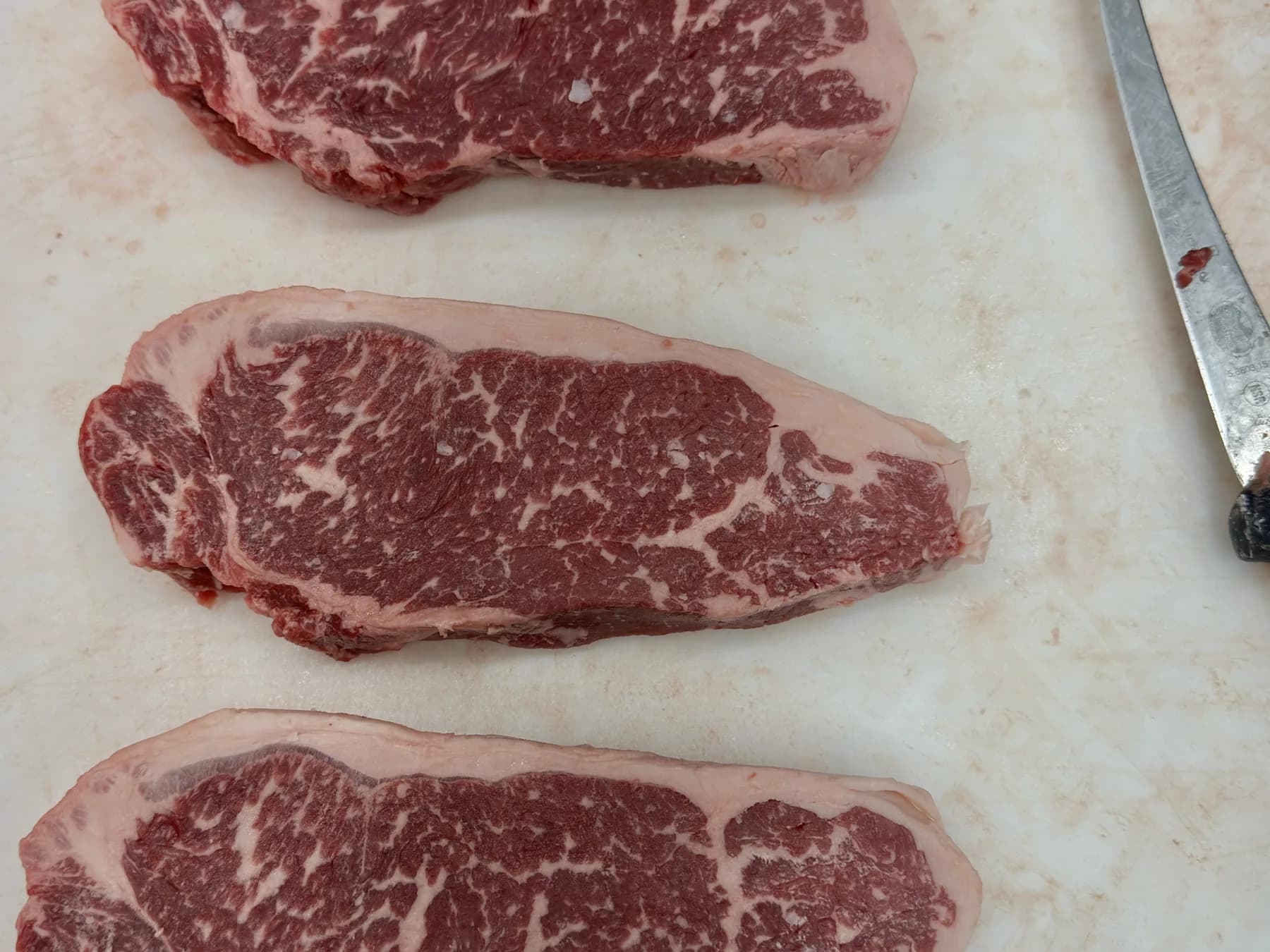 Three marbled New York strip steaks on the cutting board next to a boning knife
